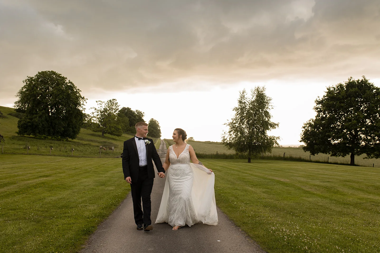 Hawkstone Hall wedding wedding day at sunset with a couple walking towards the camera. The bride holds her dress to one side and they look at each other.