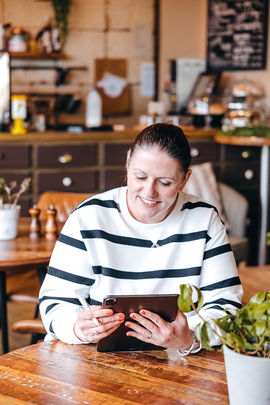 woman in coffee shop looking happy as she looks down at her iPad