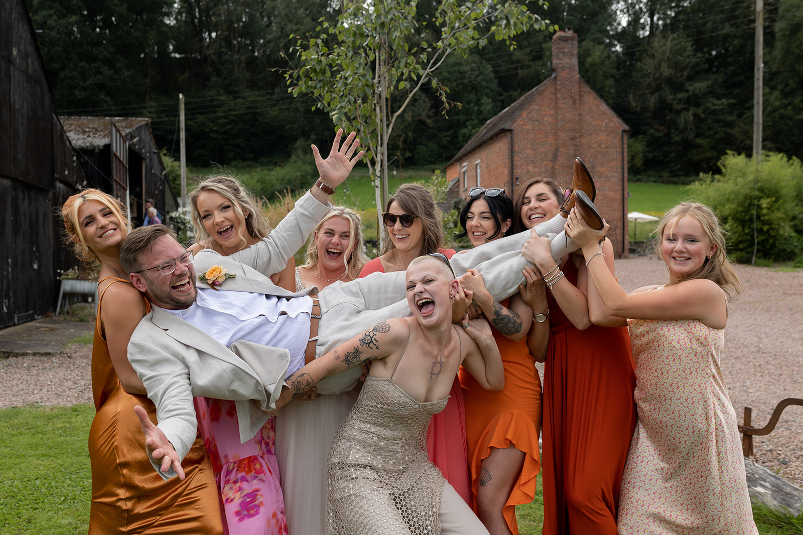 Groom being held by bridesmaids all laughing and looking happy