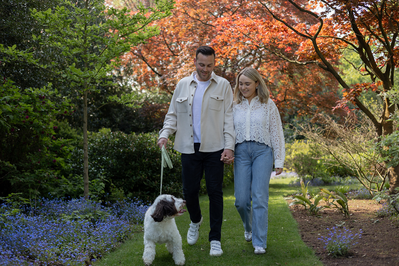 Couple walking their dog in a pretty garden looking happy