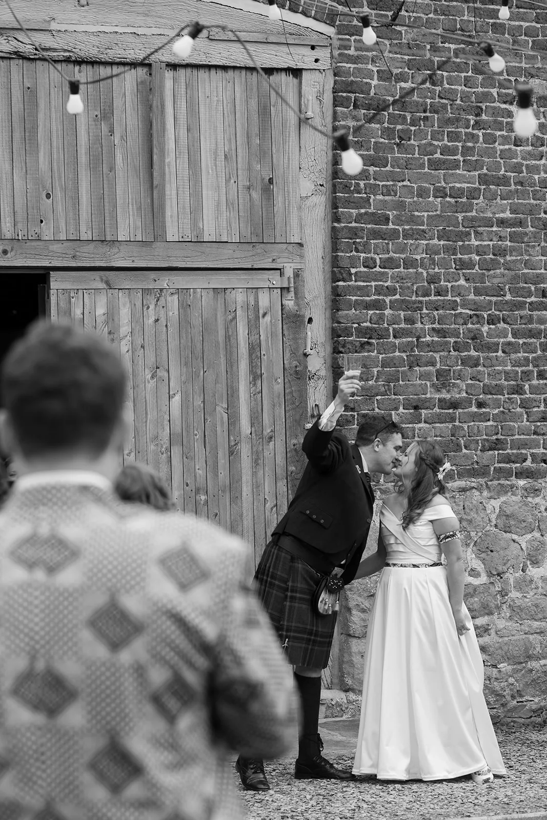 Black and white wedding photo showing a couple kissing as they raise a glass in celebration