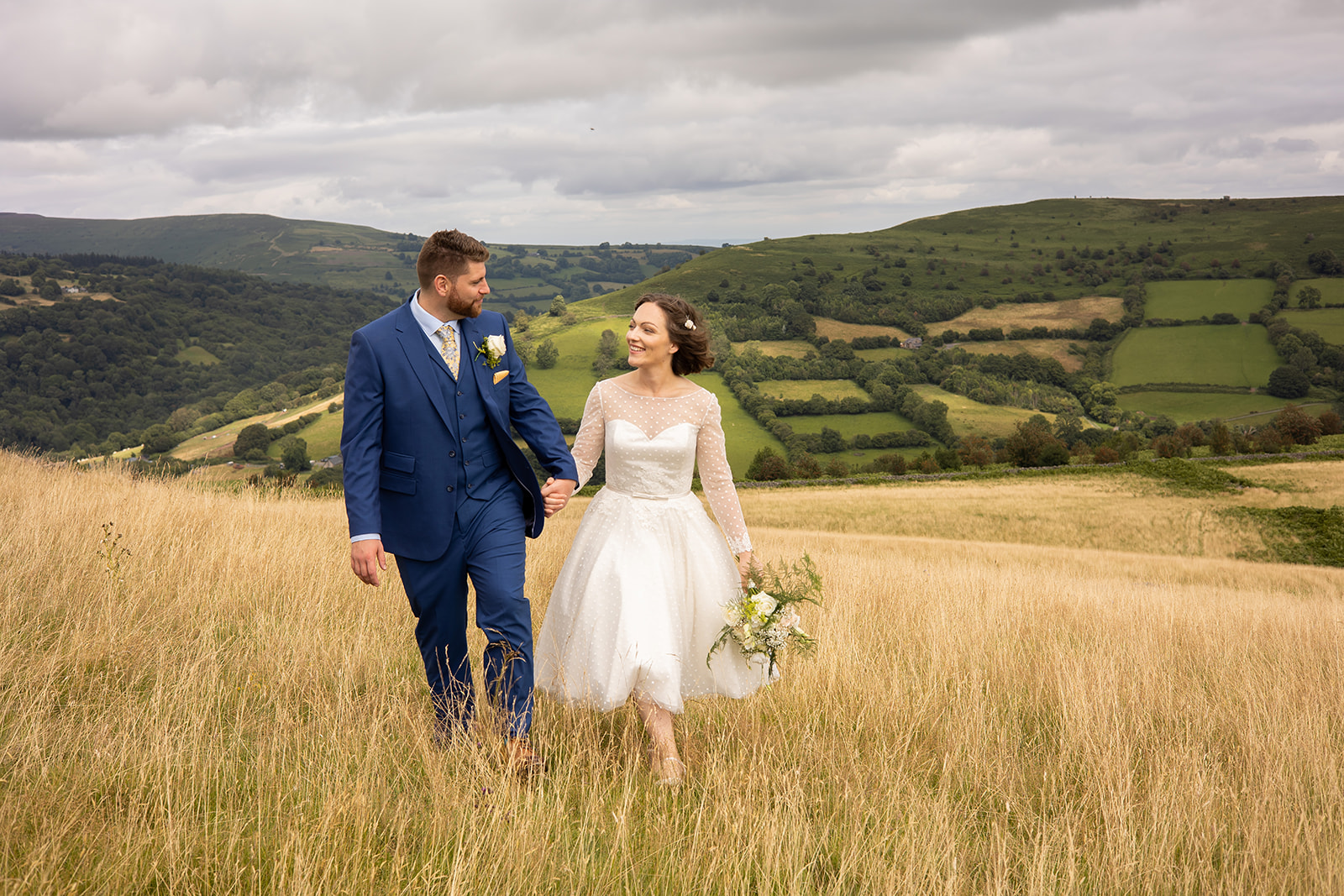 A couple on their wedding day walking up a hill looking happy. The field is golden yellow.