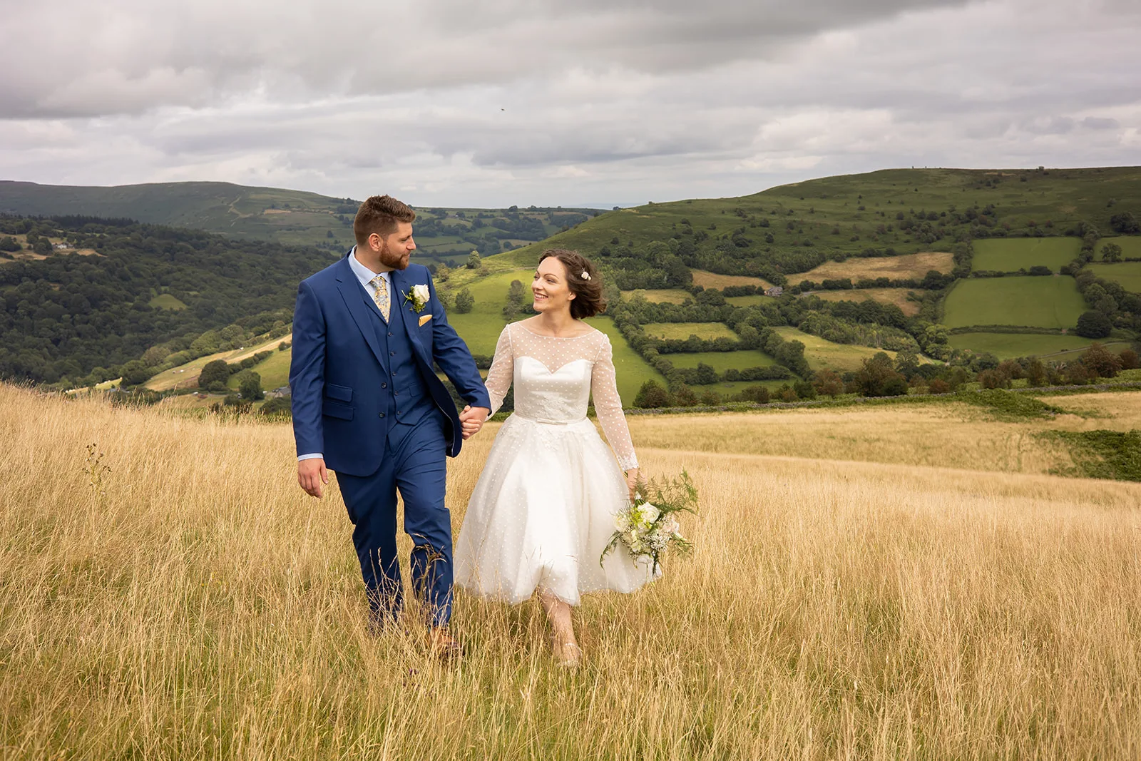 Sugar loaf barn wedding A couple on their wedding day walking up a hill looking happy. The field is golden yellow.