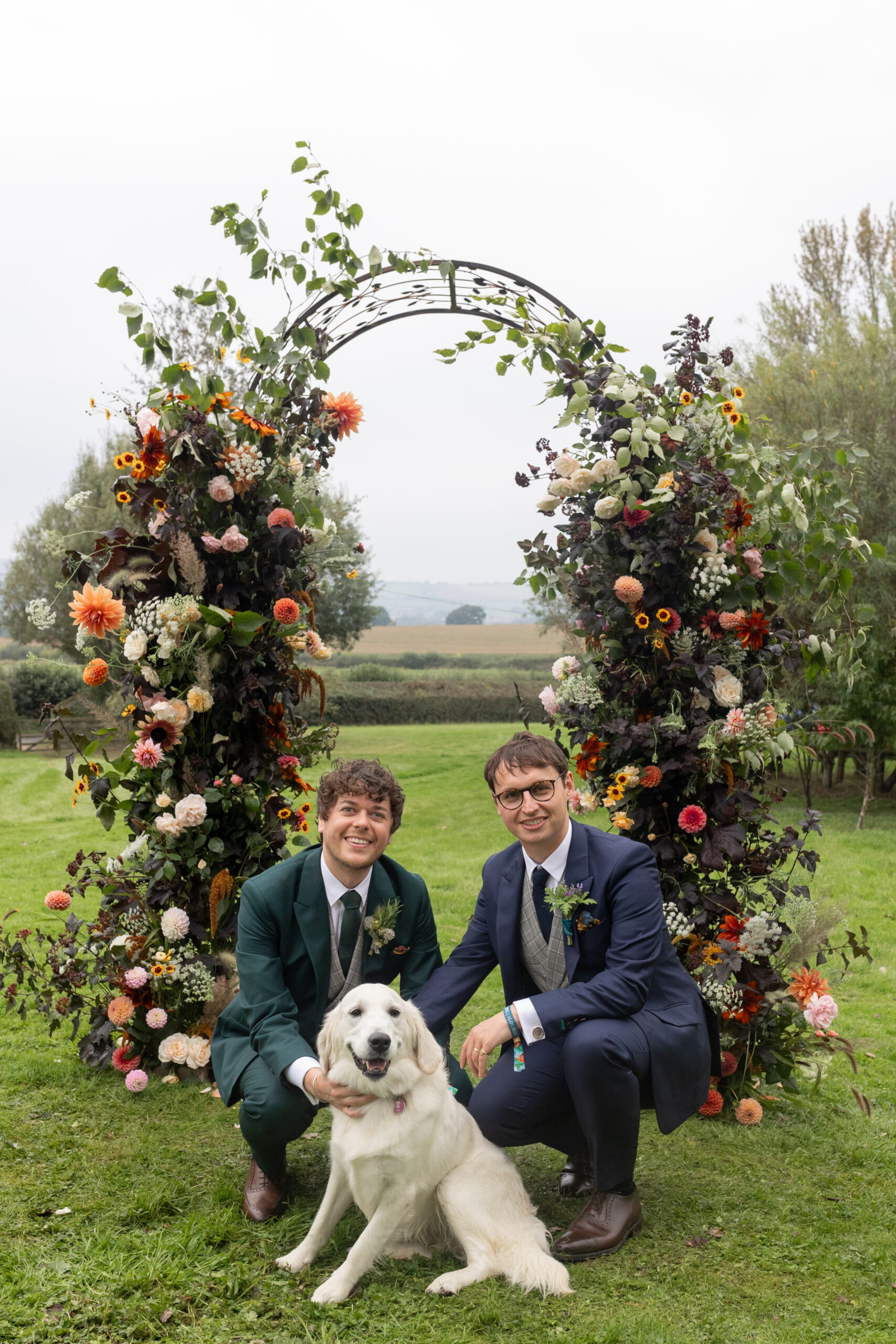 Same sex wedding of two men. They are crouched down and joined by their dog 