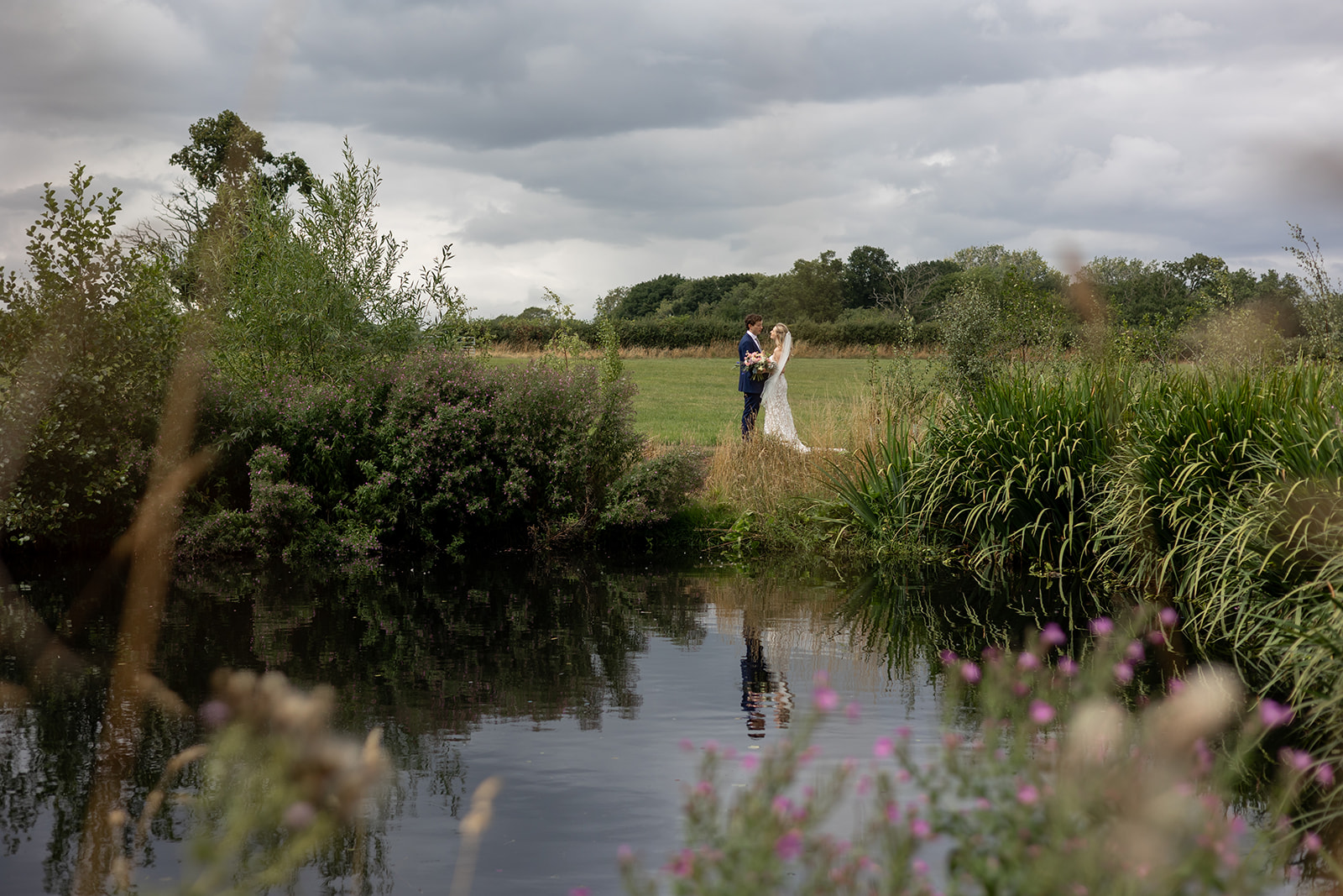 wedding photo showing a couple in the distance across a body of water with greenery all around them