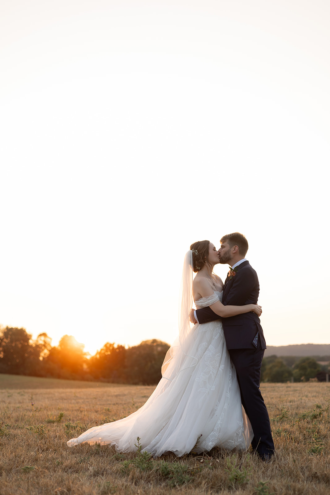 A couple kiss at sunset in a field on their wedding day